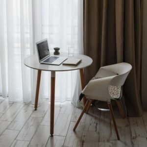 A stylish and minimalist home office setup featuring a table, chair, and laptop by large windows.